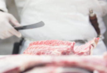 butcher's hand holding a knife about to cut rack of lamb